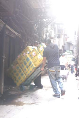 Image of a porter carrying cartons from Chungking Mansions to the quasi-legal moving trucks on the back street.