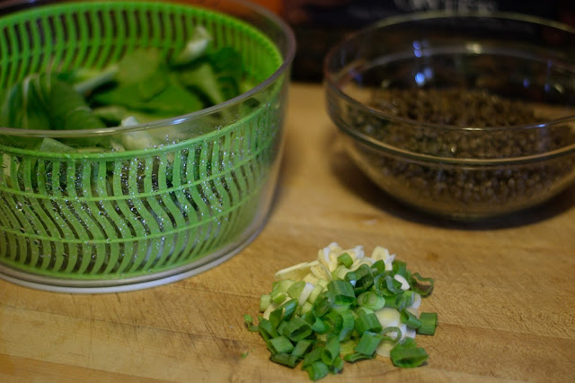 The prepared bok choy, lentils, green onions, and garlic on a cutting board.  