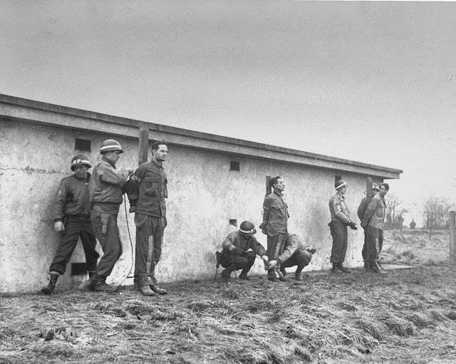 German infiltrators lined up for execution by firing squad after conviction by a military court for wearing U.S. uniforms during the Battle of the Bulge. December 23, 1944.