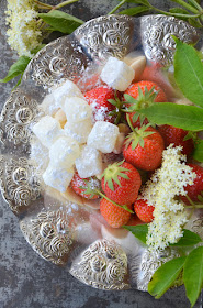 Holunderblütenkonfekt liegt zusammen mit frischen Erdbeeren und einigen Mandeln auf einem silbernen Teller.