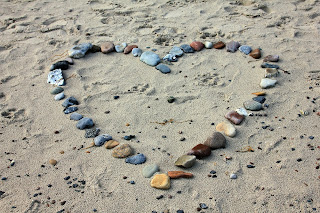 heart made out of many colored stones, on a sandy beach