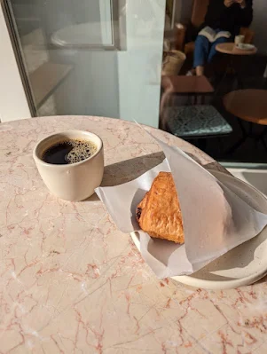 Cup of batch brew specialty coffee and a pan au chocolate sitting on a table in the sun