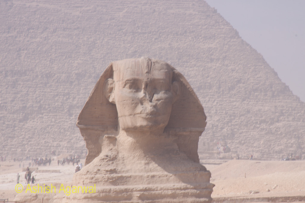 View of the full face of the Sphinx, with the structure of the Great Pyramid in the background