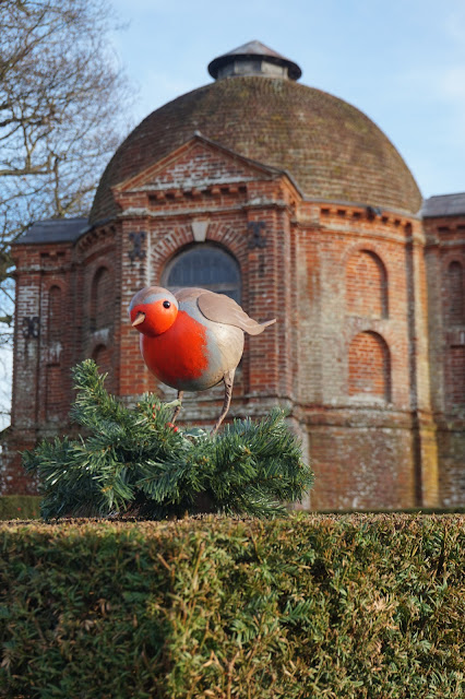 Figure of a Robin on top of a Yew Hedge with a brick building the background, in the gardens at The Vyne
