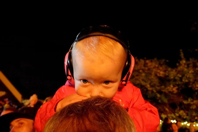 Little with ear defenders on leaning on her Daddy's head while sitting on his shoulders