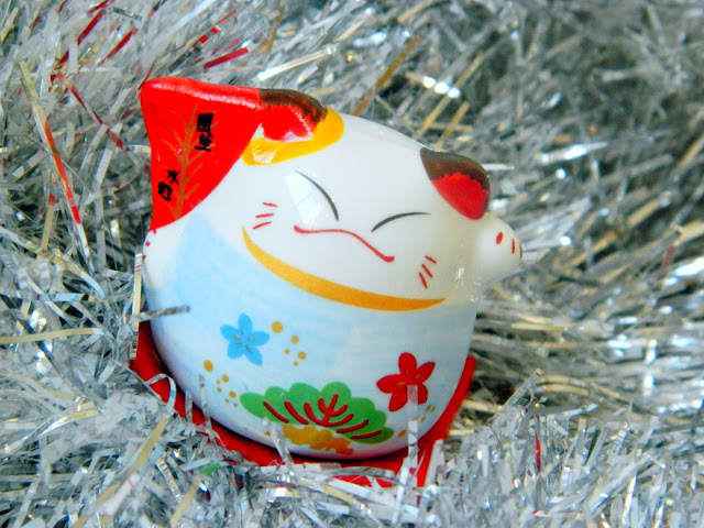 A photo showing a little ornament of a maneki neko or lucky cat. It is sitting on silver tinsel.