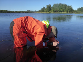 Pelastautumispukuinen henkilö katsoo vesikiikarilla pinnan alle