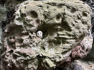 A small ceramic skull (Skulferatu 105) in a dimple in the rough rock at the top of the entrance to the Shell Grotto. Photo by Kevin Nosferatu for the Skulferatu Project.