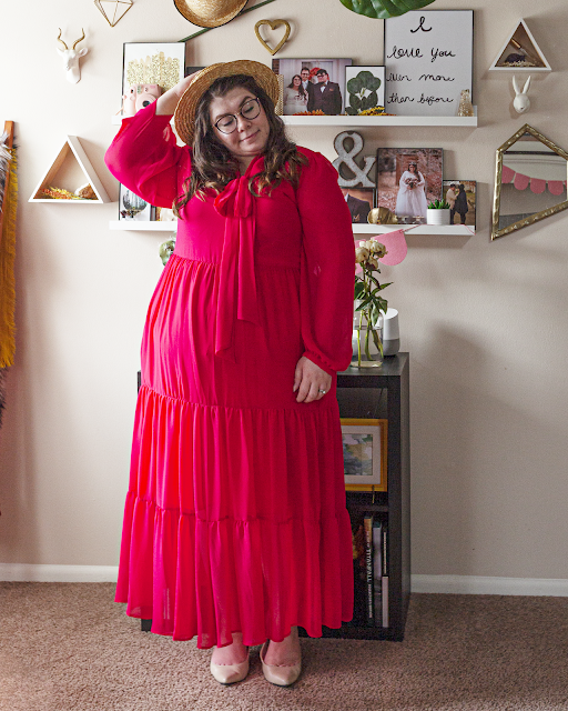 An outfit consisting of a straw boater hat, a red long bishop sleeve tiered maxi dress, and beige heels.