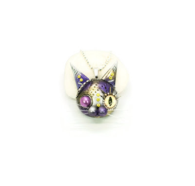 A teampunk cat's head with purple and yellow paintwork, available as a necklace