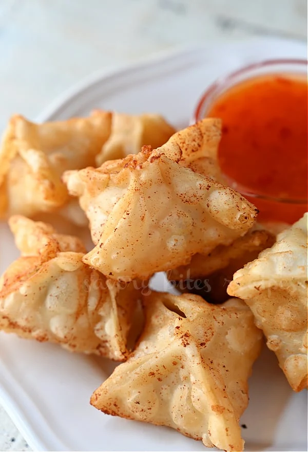 a white plate with crab rangoon with dipping sauce