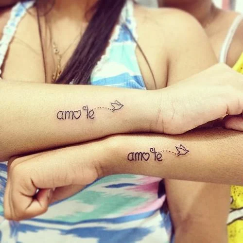 dos chicas con tatuajes de frases en sus antebrazos que dicen te amo