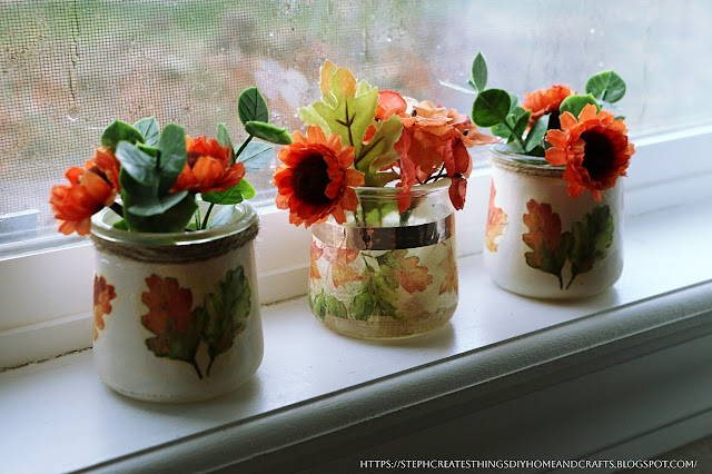 Three fall glass jar decorations displayed on a windowsill