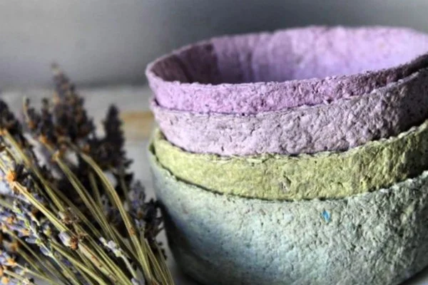 stack of four roughly textured paper bowls in shades of purple, blue, and green displayed next to sheaf of lavender