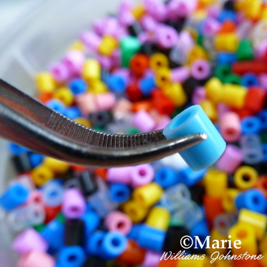 Picking up fused Perler beads with a pair of curved tweezers