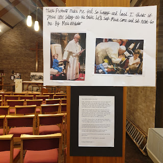 A display panel with text by Maia Webster showing Pope Francis alongside disabled children.
