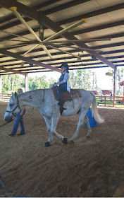 Bryanna rides a white horse with light grey spots. It's being led by somebody outside of the picture's frame