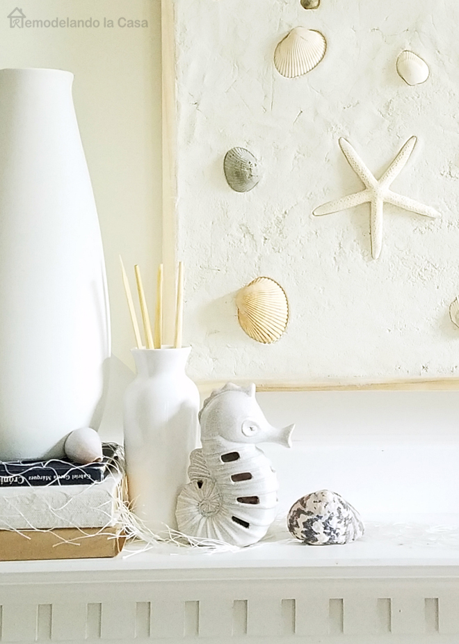 sea shells wall art on mantel with white vase and wooden fish