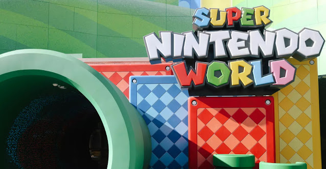 Imagem da entrada do Super Nintendo World na Universal Studios Hollywood. Há o letreiro com o nome da área e um cano gigante pelo qual visitantes entram.