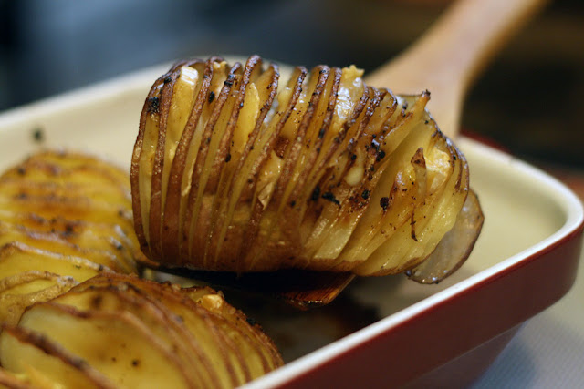 A square dish with a Hasselback Potato stuffed with brie cheese being lifted out. 