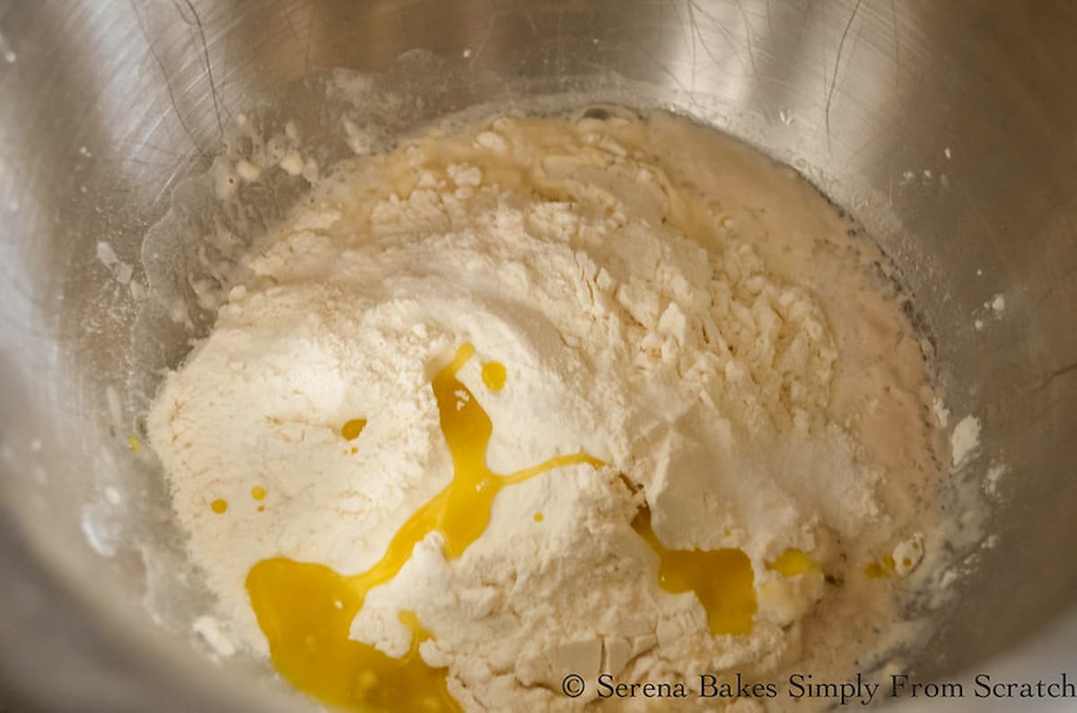 Flour, Salt, and Olive Oil added to yeast mixture in a stainless steel mixing bowl.