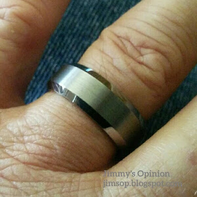 A gray tungsten wedding band with beveled edges being worn on the left ring finger of my hand.