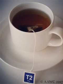 A white cup and saucer with a T2 teabag dangling inside it.