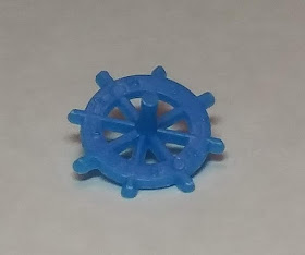 A small blue plastic top, of the type that often comes as a prize in cracker jack boxes. The horizontal part of the top looks like the steering wheel of a pirate ship, with eight spokes running from the centre to extend beyond the circle. It's hard to see, but there are raised numbers on the wheel between each spoke.