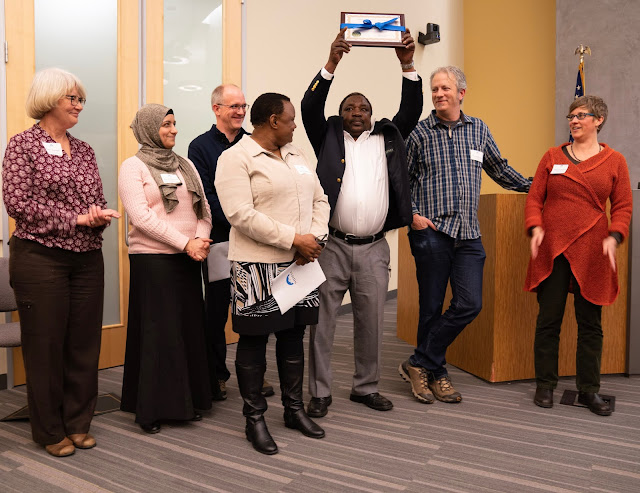 Standing with a group of 8 men and women, Stanley jubilantly holds their certificate over his head while they all laugh and smile at him