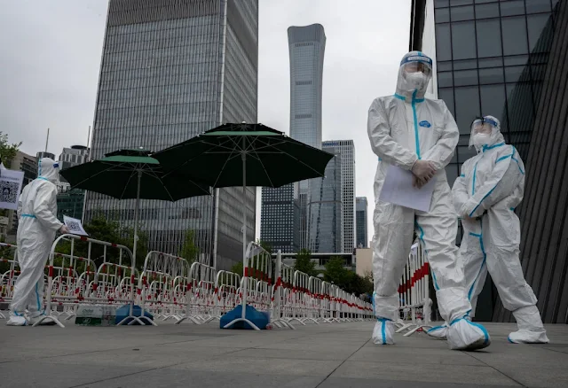 Image Attribute: Health workers wear protective suits while waiting to register office workers for COVID-19 tests in Beijing on April 27. | Source: Kevin Frayer / Getty Images