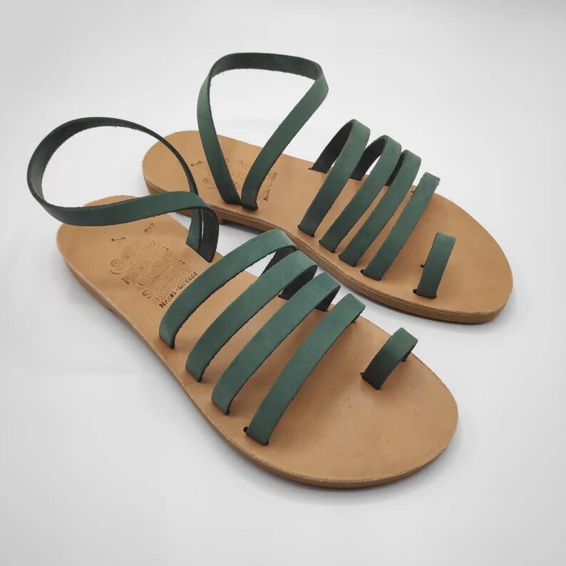 A pair of sandals on a plain white background. The sandals are low, with 4 straps on the foot and a strap that starts from the inside of the foot, passes around the ankle and returns to the starting point, sage green, except for the insole which is leather.