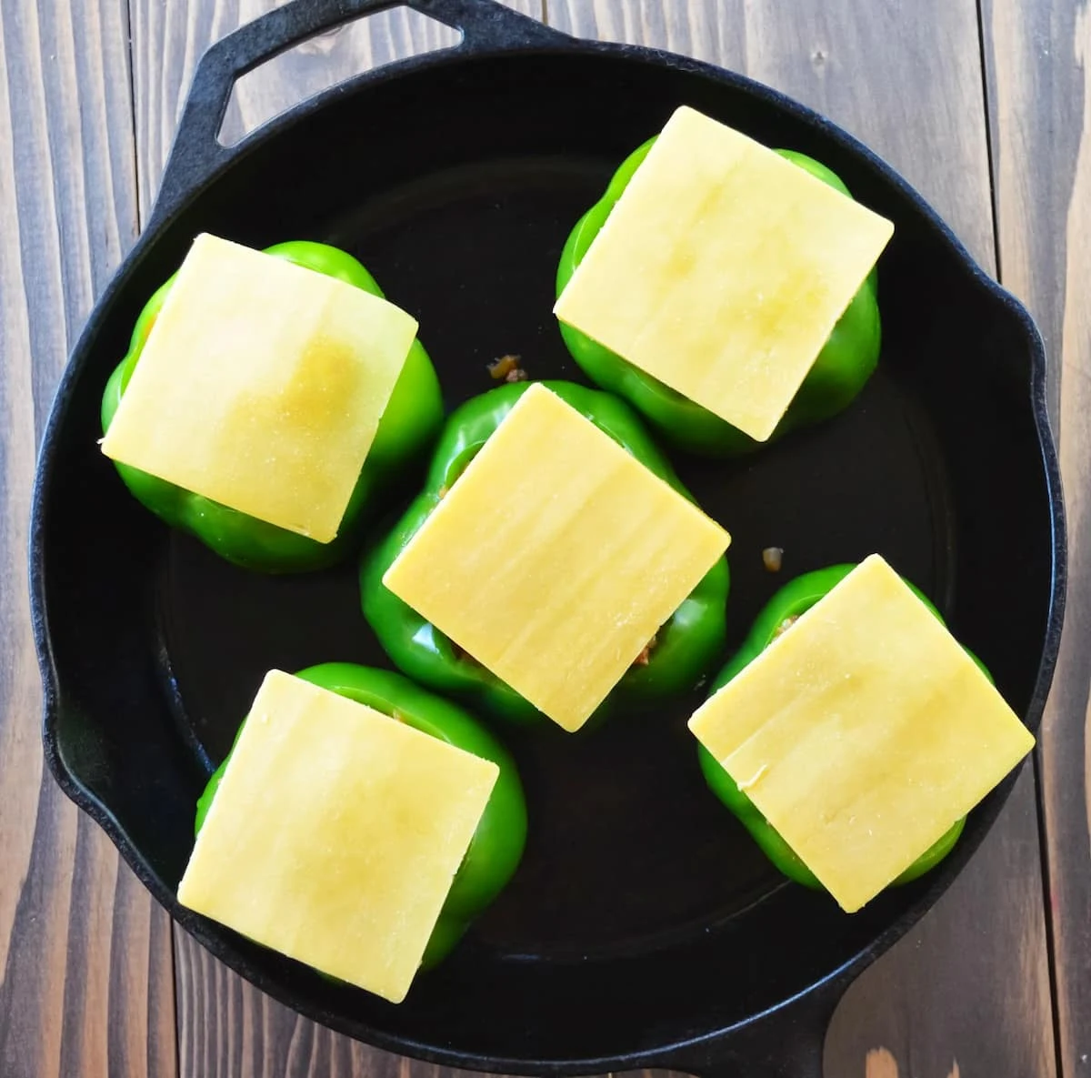 Uncooked Stuffed Bell Peppers topped with slices of Cheddar Cheese.