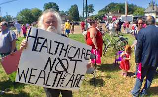 Michael Heinrich with a protest sign: Healthcare not wealthcare