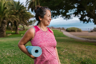 An older woman holding a yoga mat.