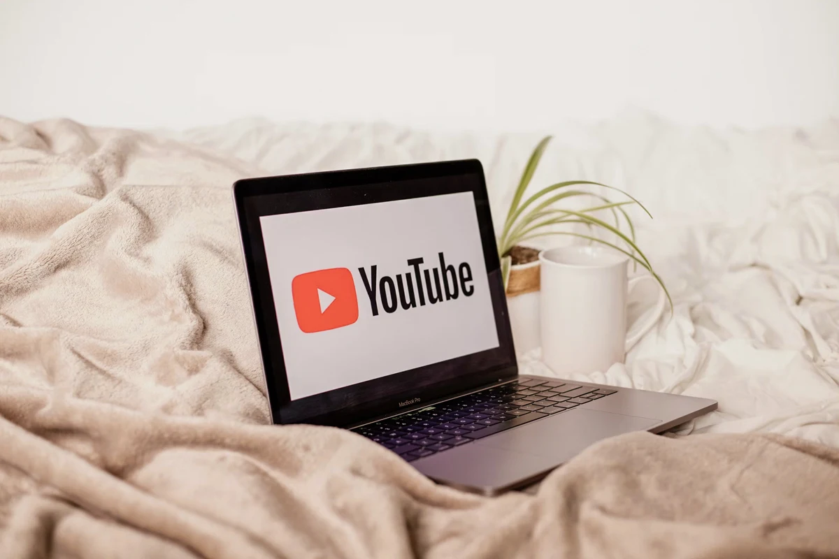 an opened laptop with an opened youtube app on top of a bed