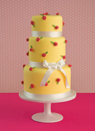 Three tier round draping wedding cake in yellow with an abundance of fresh