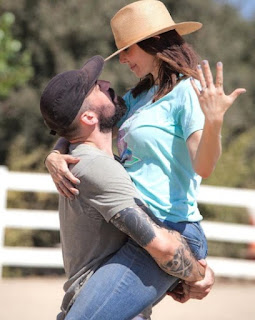 Whitney Cummings showing engagement ring while carried by Miles Skinner