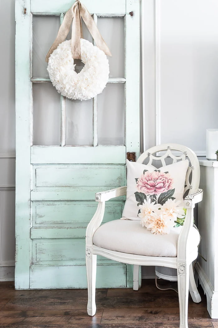 coffee filter wreath hanging on vintage chippy door, white chair and pillow