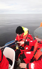 Kaksi pelastuspukuista henkilöä tutkii kameraa veneessä.