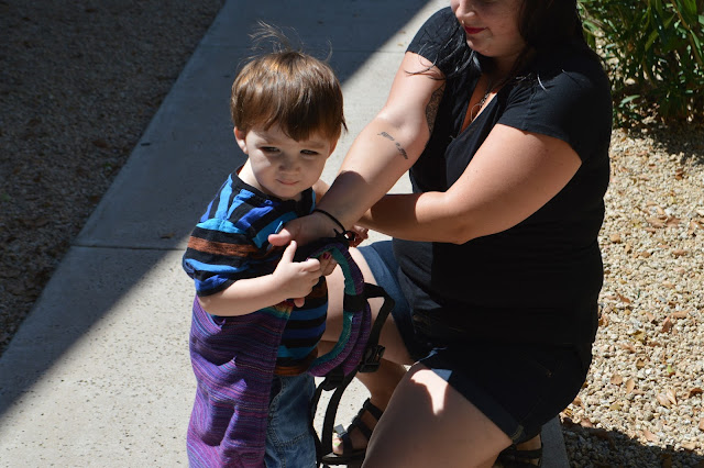 Image of fair skin, dark haired woman with arms crossed holding shoulder straps and toddler's shoulders