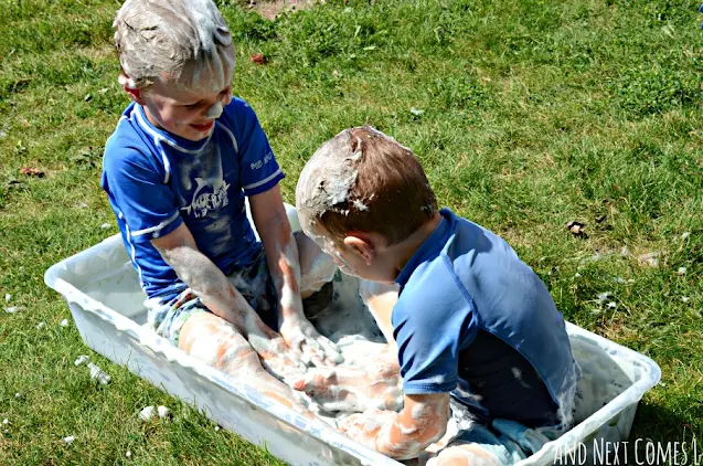 Kids sitting in a sensory bin filled with soap foam bubbles