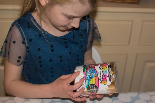 A girl looking at the round tub like packaging of Poopsie Slime Surprise Poop Pack Drop 2