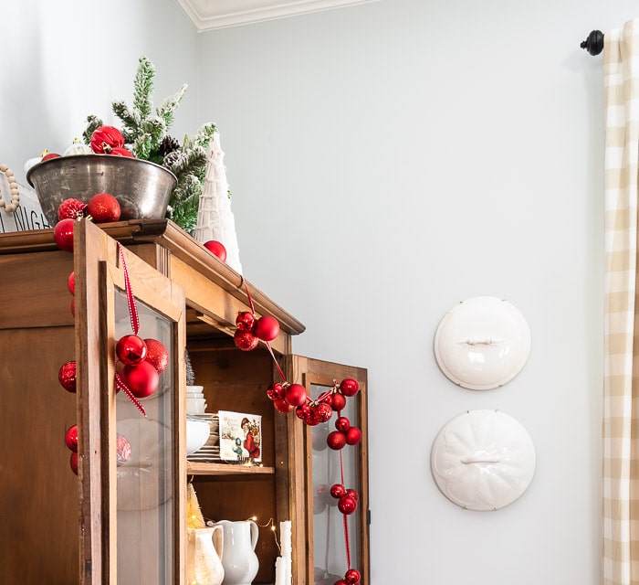 red ornament garland draped over pine hutch doors, ironstone lids hanging on wall