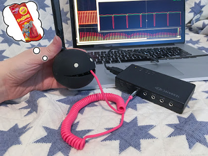 [Image: A Black Otamatone with a cable coming out of its mouth into a USB sound card. A waveform with more binary nature is displayed on a screen.]