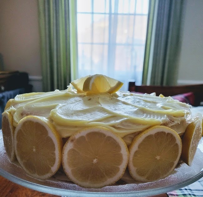 Lemon cake on glass cake stand on top of wood table 