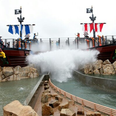 Two Pirate Ships with a bridge between them, a wall of water splashing water onto bridge and hiding view of boat in water flume.