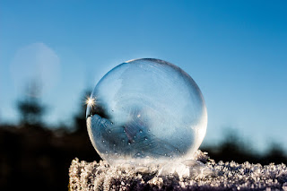 A frozen bubble rests on a frosty stone or log, catching the light.