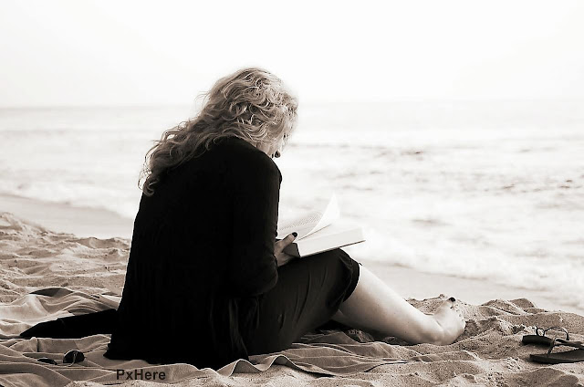 Mulher lendo livro na praia junto ao mar.