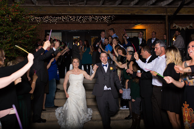 Their guests gather around as the newlyweds make their way through the crowd saying "goodbye."  In celebration, the guests are waving colored glow sticks.  May the husband and wife have a long, happy marriage together!  Set at the Hall at the Railhouse located in Norman, OK during the fall of 2016.