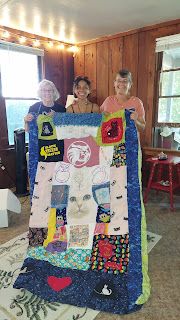 3 women standing behind a homemade quilt.